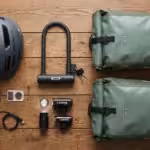 Essential bicycle commuting equipment like a helmet, lock, and bags neatly arranged on wood.