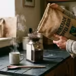 A person pours Fairtrade coffee beans from a burlap sack into an electric grinder.