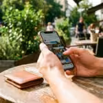 Close-up of hands scrolling through photos on a smartphone at an outdoor cafe table.