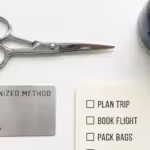 Flat lay of silver scissors, a succulent, metal card, and travel checklist on white background