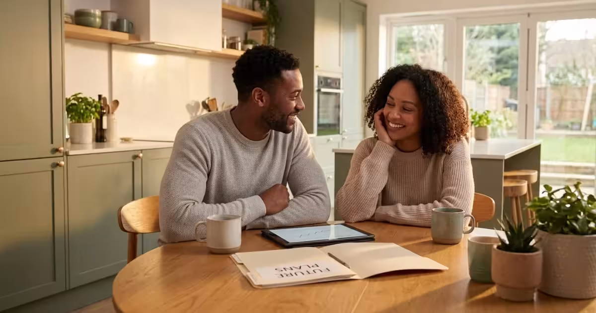 Smiling Black couple sitting at a kitchen table discussing future plans with a tablet