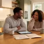 Smiling Black couple sitting at a kitchen table discussing future plans with a tablet