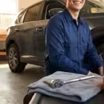 Smiling man in a blue shirt prepares for an oil change in his garage.
