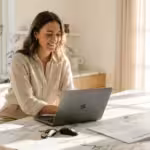 Smiling woman working on a laptop at a bright marble kitchen island with a contract.