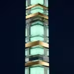 A vertical stack of glowing mint green glass cubes separated by polished gold metallic bands.