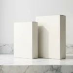 Two plain white cardboard product boxes standing on a white marble countertop near a window