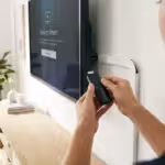 Woman inserting a black media streaming device into the side of a wall-mounted smart television.